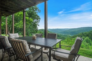A covered outdoor seating area with a table and chairs, overlooking a forested valley. - Wooded Cabin Charm, Lake Views, Hot Tub, Fire pit (New Tazewell)