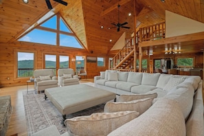 A spacious living area with a large sofa, a coffee table, and a view of the outdoors. - Serene Mtn Cabin Retreat,  Lake Views , Hot Tub (New Tazewell)