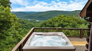 Un jacuzzi en una terraza de madera con vistas a un valle boscoso y un río.