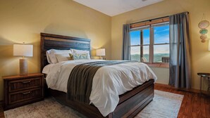 Une chambre à coucher avec un grand lit, deux tables de chevet, une fenêtre avec des rideaux et une vue sur l’extérieur.