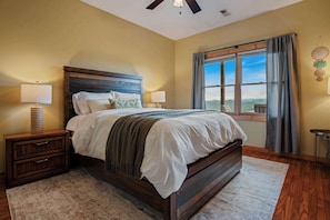 A bedroom with a large bed, two bedside tables, a window with curtains, and a view of the outdoors. - Serene Mtn Cabin Retreat,  Lake Views , Hot Tub (New Tazewell)