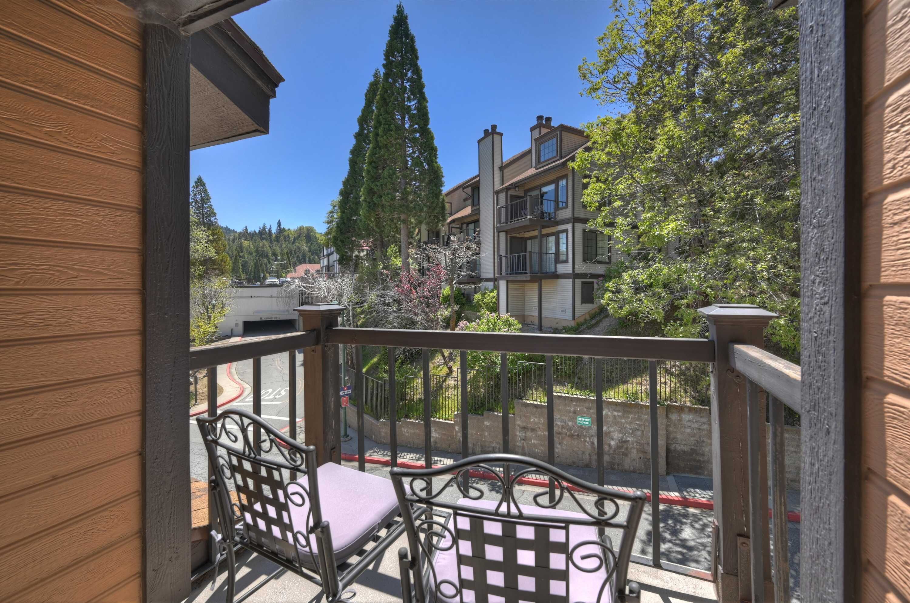 A balcony with two chairs, a railing, and a view of a multi-story building and trees.