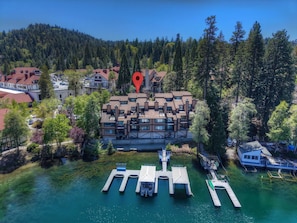 An aerial view of a modern hotel with multiple floors, a dock with boats, and a forested backdrop.