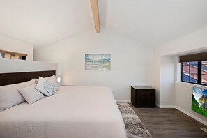 A bedroom with a bed, a nightstand, a window, and a painting on the wall.