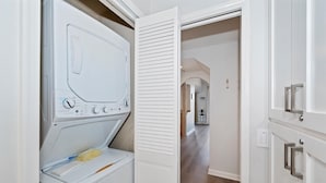 A laundry room with a front-loading washer and dryer, a door leading to a hallway, and a light switch on the wall.