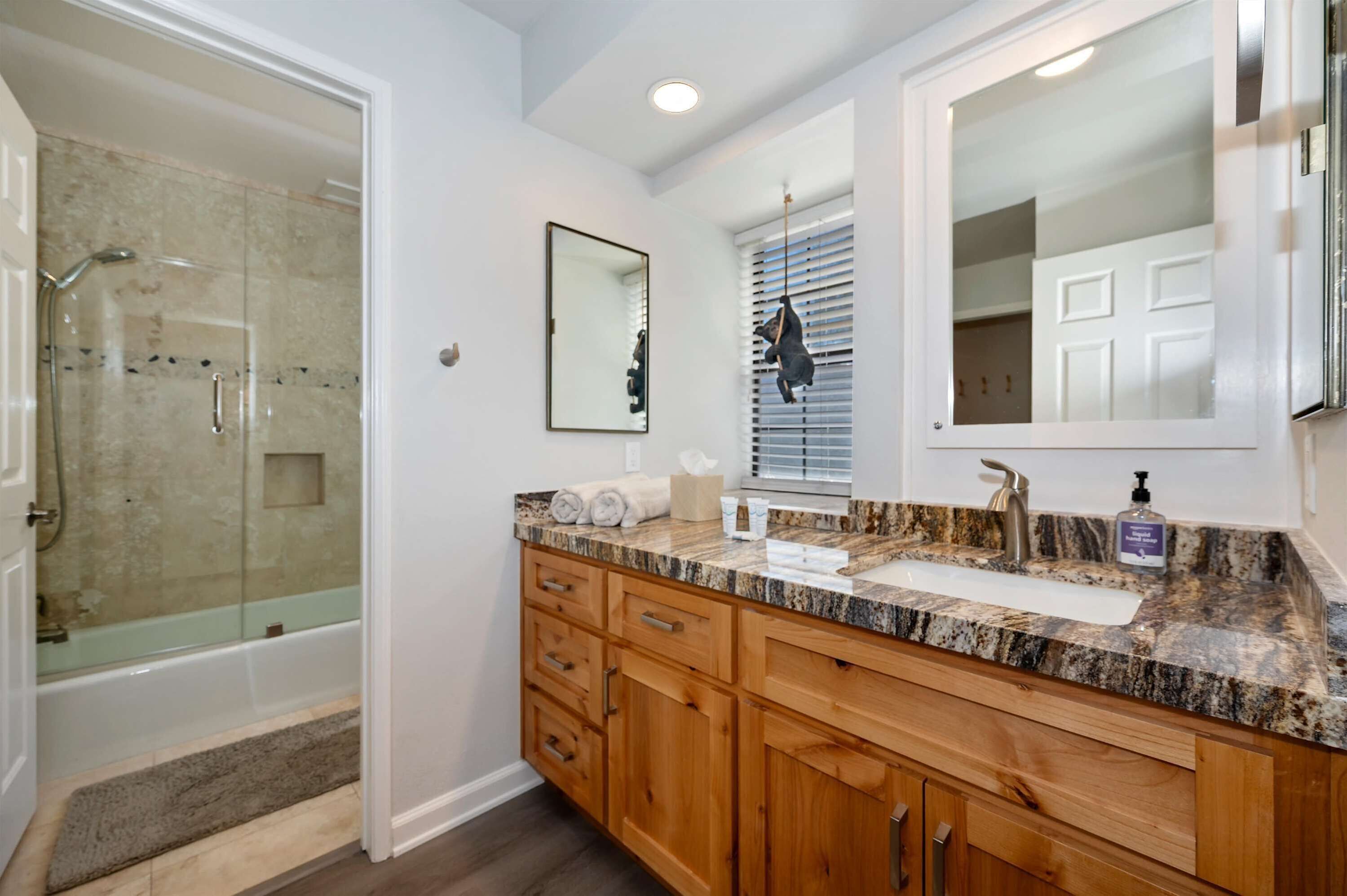 A modern bathroom with a glass shower, wooden cabinets, a marble countertop, and a large mirror.