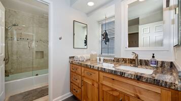 A modern bathroom with a glass shower, wooden cabinets, a marble countertop, and a large mirror.