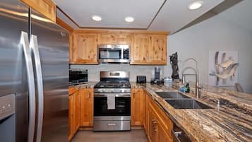 A modern kitchen with wooden cabinets, stainless steel appliances, granite countertops, and a granite backsplash.