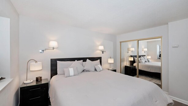A hotel room with a bed, bedside lamps, a nightstand, a mirror, and a wardrobe.