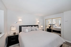 A hotel room with a bed, bedside lamps, a nightstand, a mirror, and a wardrobe.