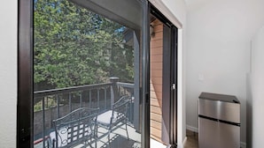 A balcony with a metal railing, a bench, and a stainless steel refrigerator.
