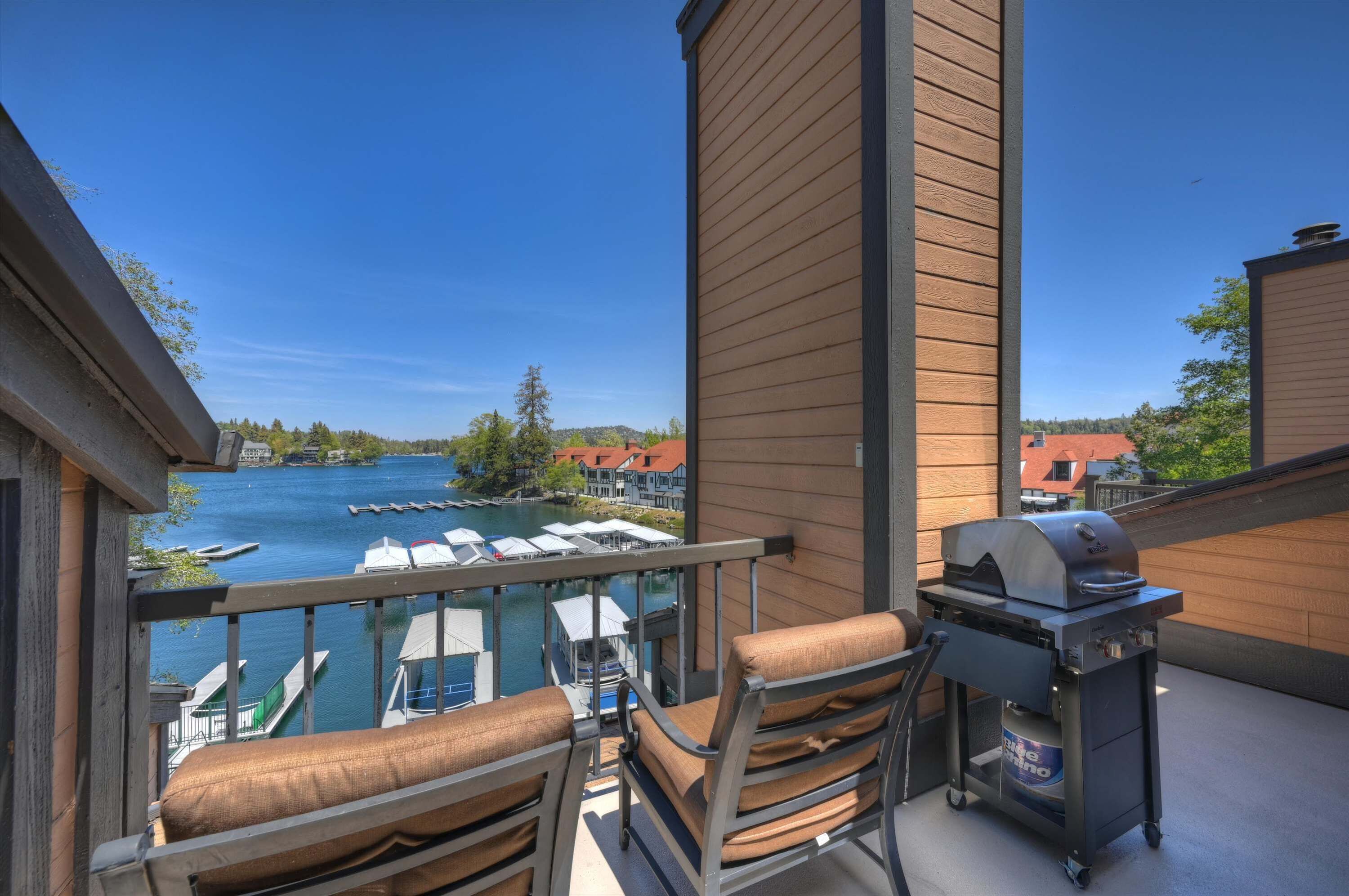 Ein Balkon mit Grill, Stühlen und Blick auf einen See mit Booten.