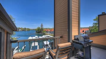 Een balkon met een barbecue, stoelen en uitzicht op een meer met boten.