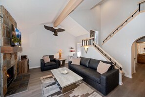 Una sala de estar con chimenea de piedra, un sofá, una mesa de centro y una escalera.