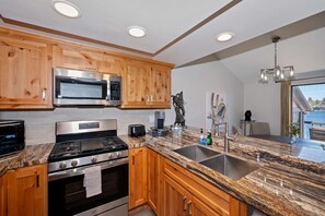 Una cocina moderna con gabinetes de madera, electrodomésticos de acero inoxidable, encimeras de granito y un ventanal grande.