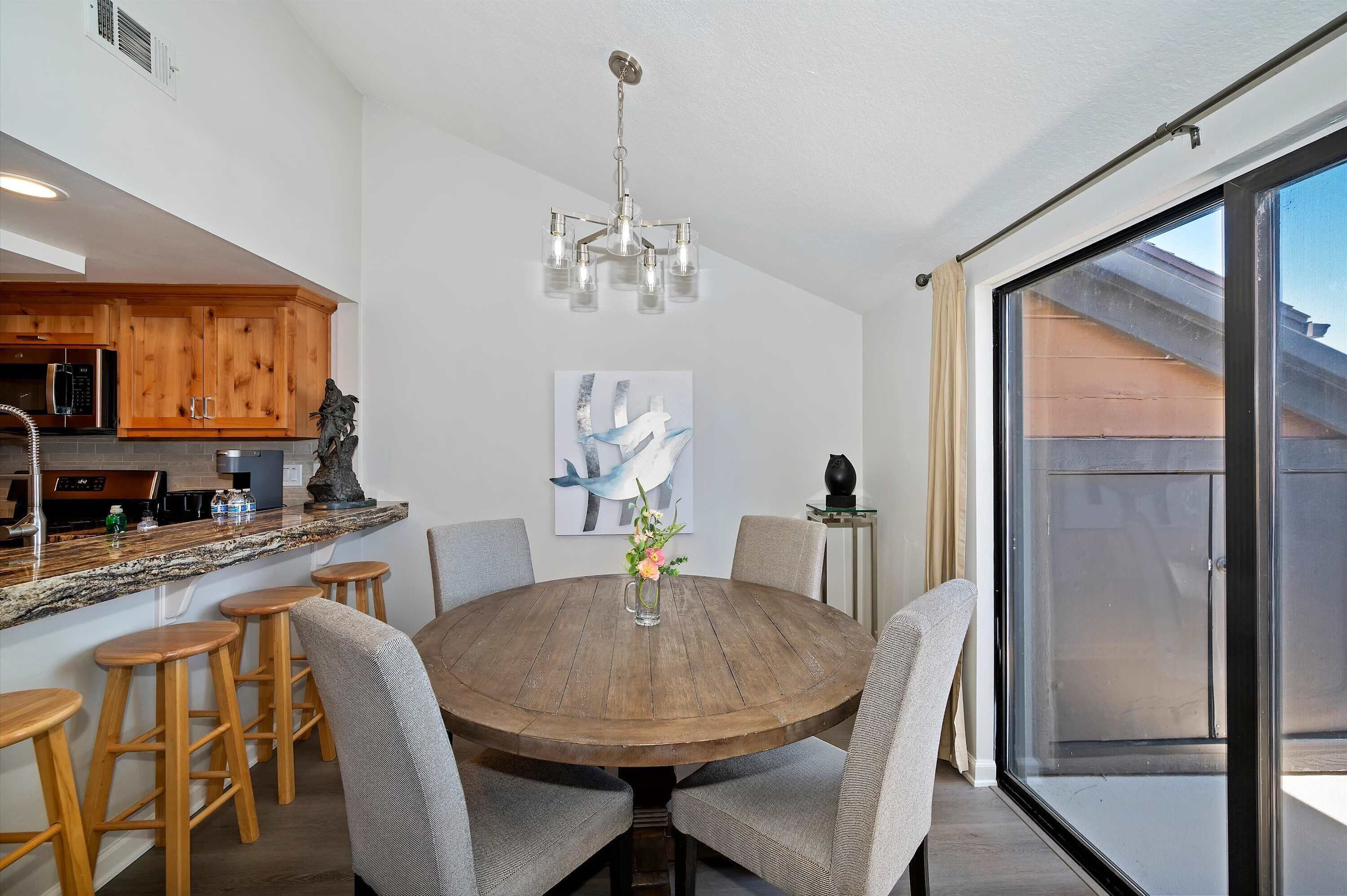 A round wooden dining table with bar stools, a chandelier, and a painting on the wall.