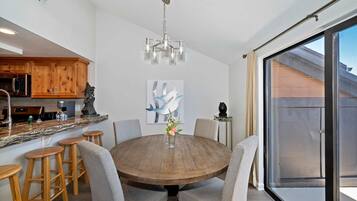 A round wooden dining table with bar stools, a chandelier, and a painting on the wall.
