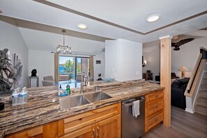 Una cocina moderna con encimeras de granito, un lavamanos de acero inoxidable, armarios de madera y vistas al exterior.