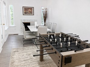Una habitación moderna con mesa de fútbol, zona de comedor con mesa de mármol y chimenea.