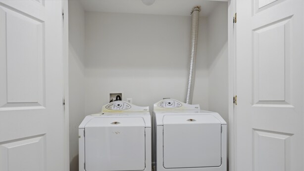 A laundry room with two white washing machines and a hose.