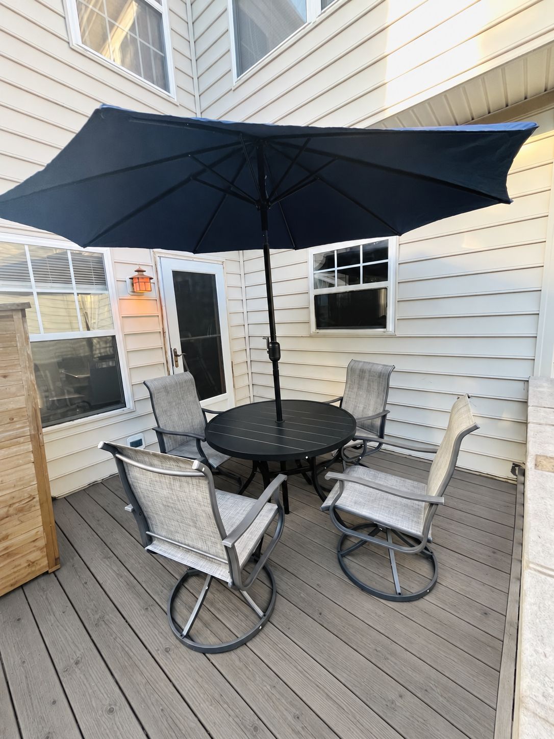 An outdoor patio with a round table and four chairs, an umbrella, and a lantern.