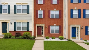 A row of three-story townhouses with front doors, windows with shutters, and a small lawn area.