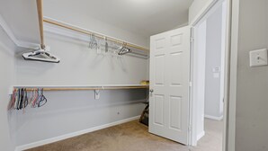 A walk-in closet with a wooden rod and multiple hangers, a white door, and a light switch on the wall.