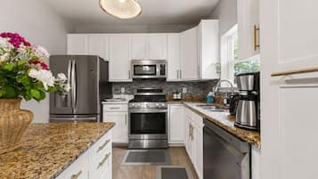 A modern kitchen with white cabinetry, stainless steel appliances, a granite countertop, and a hanging light fixture.