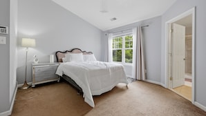 A bedroom with a bed, nightstand, lamp, window, and door.