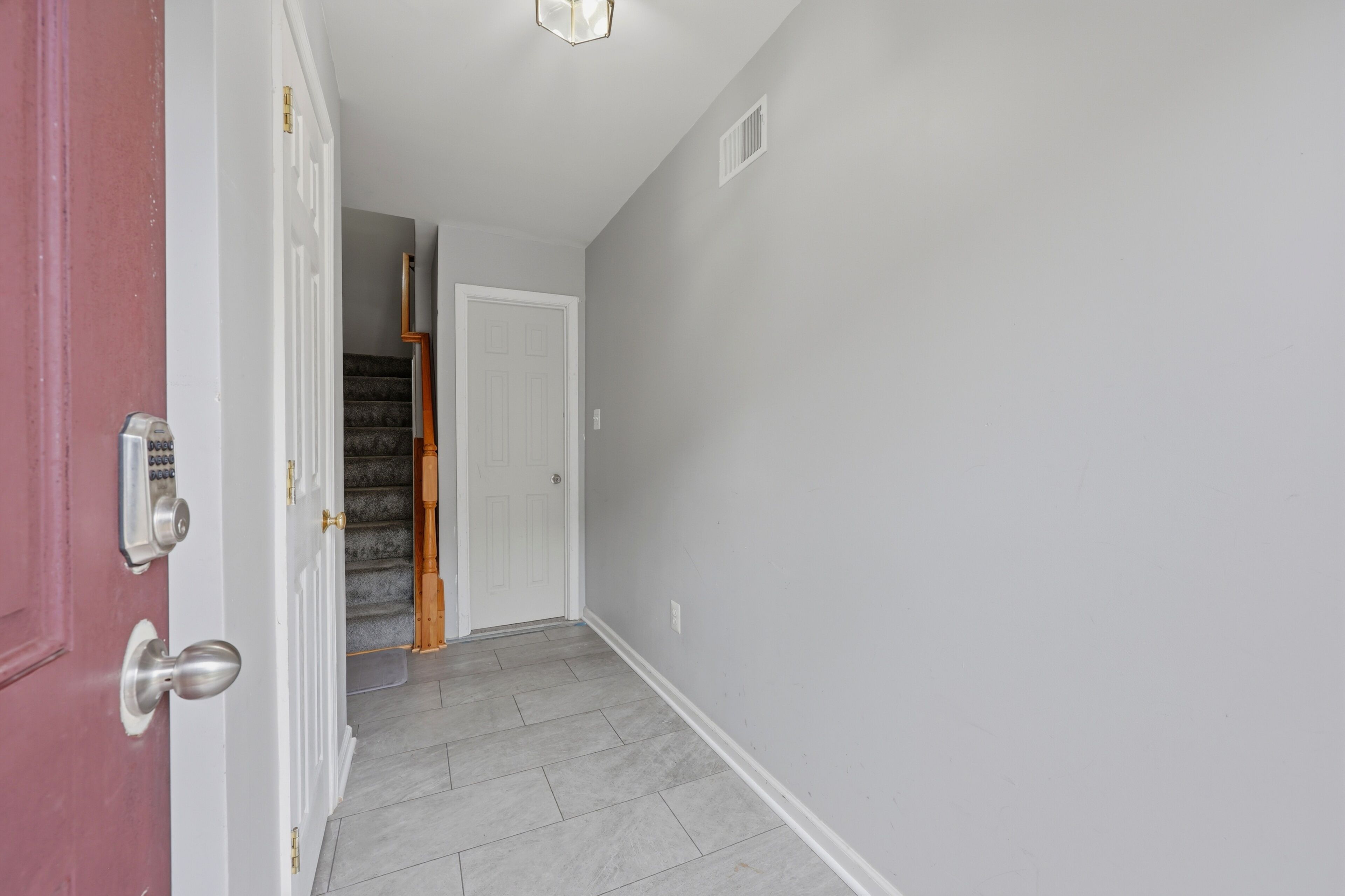 A hallway with a red door, a white door, and a staircase leading to another room.