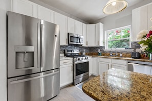 A modern kitchen with stainless steel appliances, white cabinetry, and a granite countertop.