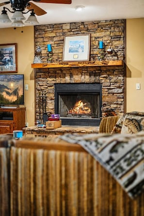 A living room with a stone fireplace, a ceiling fan, and a framed picture above the fireplace. - Lakeside Haven: Boat Dock, Ramp, Games, & MORE! (Sevierville)