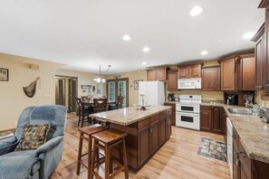 A spacious kitchen with wooden cabinets, a central island, and a dining area with chairs. - Lakeside Haven: Boat Dock, Ramp, Games, & MORE! (Sevierville)