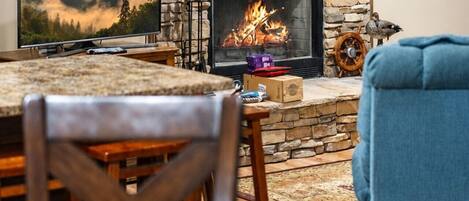 Una sala de estar con chimenea de piedra, televisor y cuadros en la pared.