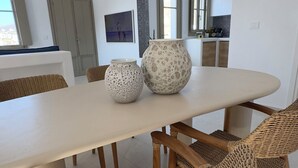 Moderni ruokailutila, jossa on suuri pöytä, rottinkituolit ja kaksi koristeellista maljakkoa.