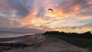 Uma praia com uma pessoa andando de scooter, um balão e um pôr do sol.