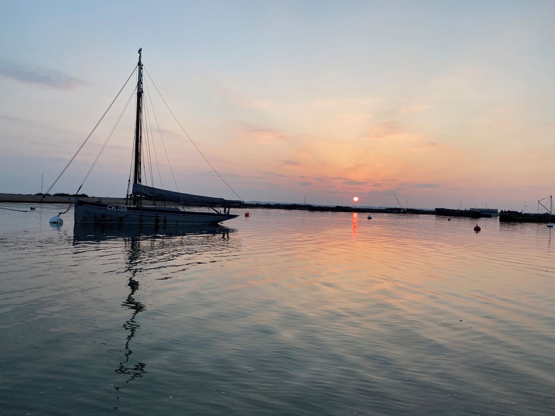 Un plan d’eau calme, avec un voilier amarré sur la gauche.