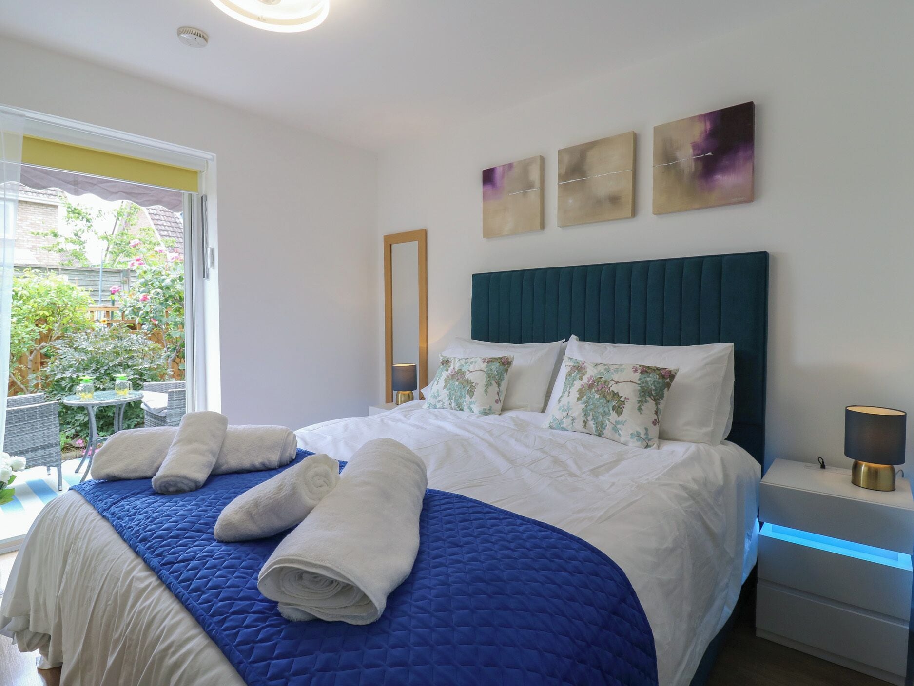 A bedroom with a bed, a nightstand, a lamp, a mirror, and artwork on the wall.