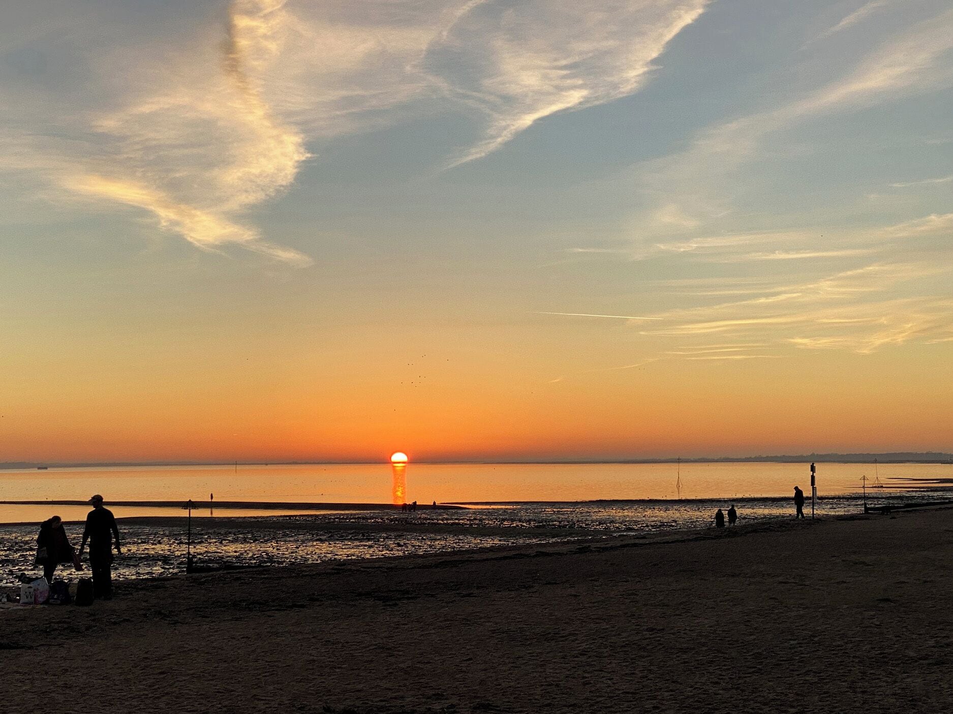 Une plage au coucher du soleil, avec des silhouettes de personnes et un bateau.