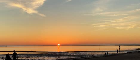 A beach at sunset with silhouettes of people and a boat.