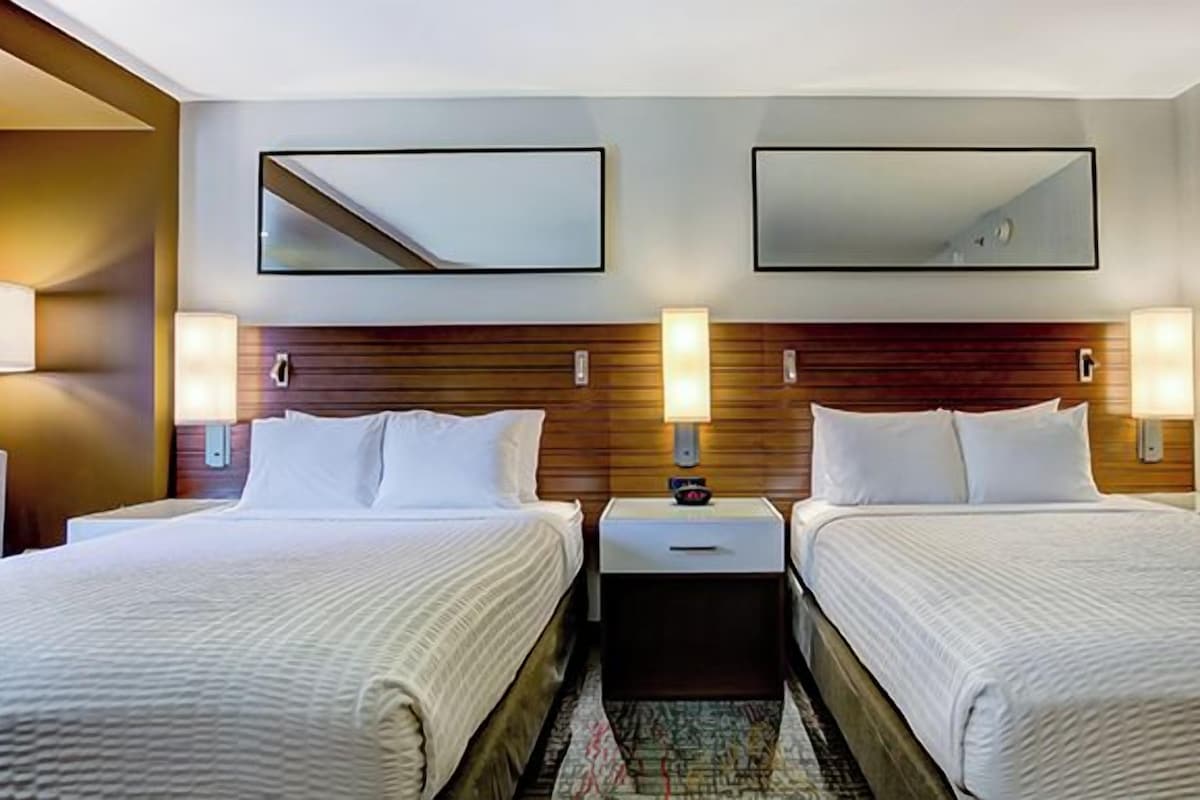 Una camera d'albergo con due letti, comodini, lampade a parete e uno specchio.