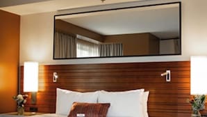 A hotel room with a large bed, a wooden headboard, a nightstand with a lamp, and a mirror above the bed. - The Point Casino and Hotel (Kingston)