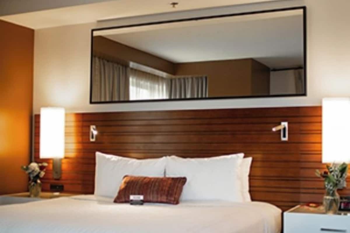 Una camera d'albergo con un letto grande, una testiera in legno, un comodino con una lampada e uno specchio sopra il letto.