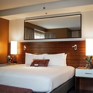 Una camera d'albergo con un letto grande, una testiera in legno, un comodino con una lampada e uno specchio sopra il letto.