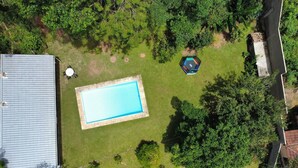 Ett flygbildsbild av ett bostadsområde med en rektangulär swimmingpool omgiven av gräs, träd och en liten lusthus.
