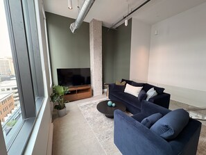 Een moderne woonkamer met een groot raam, een flatscreen televisie, een donkerblauwe bank en een salontafel.