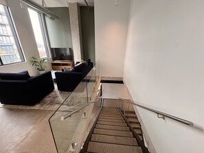 Een modern interieur met een trap, zwarte banken, een televisie en een plant.