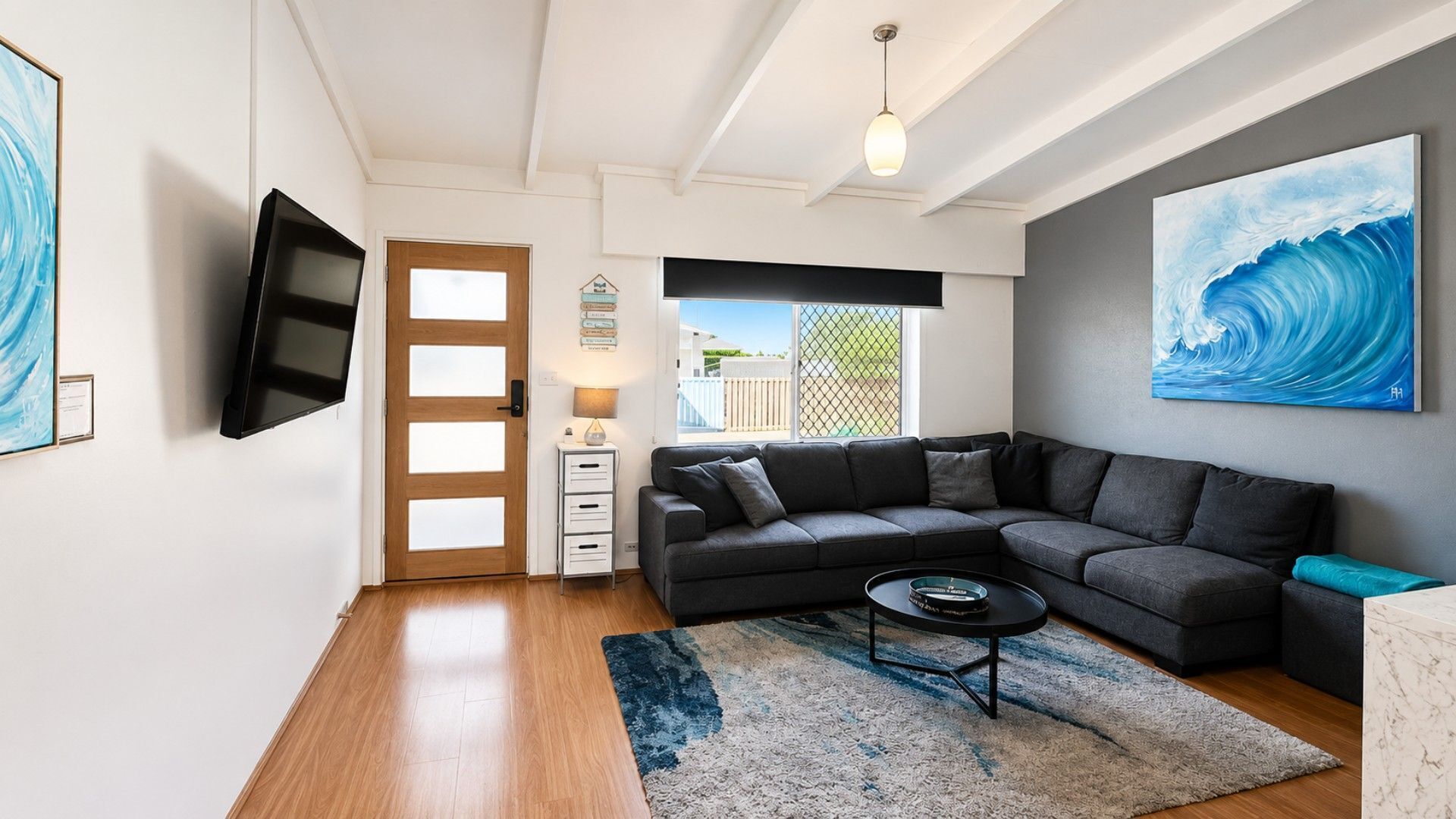 A modern living room with a sectional sofa, a flat-screen TV, a coffee table, and artwork on the walls.