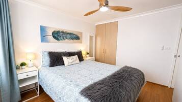 A bedroom with a bed, a nightstand, a lamp, a painting, a wardrobe, and a ceiling fan.