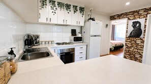 Una cocina moderna con armarios blancos, microondas integrado, cafetera y refrigerador.